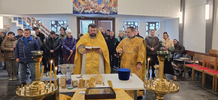 Священники біля столу зі свічками й водою, громада стоїть півколом